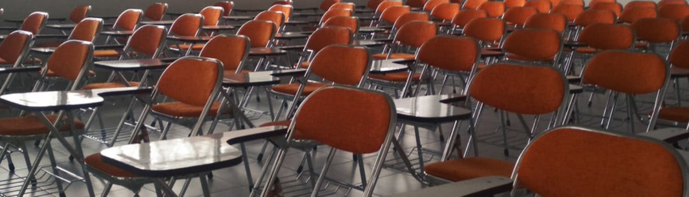 An empty classroom full of desks with orange chairs attached to them