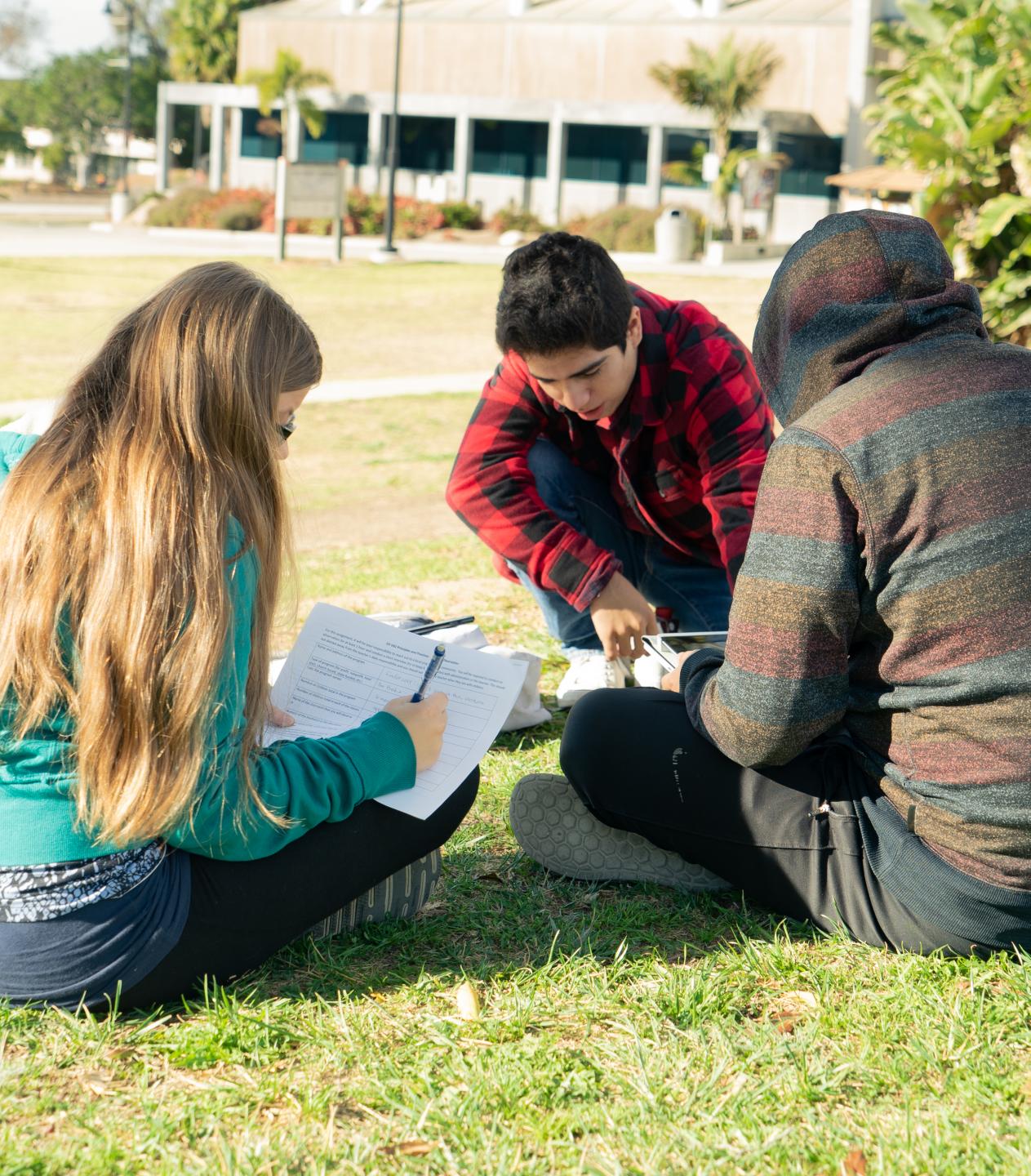 three students in a study group sitting on the grass at ventura college.