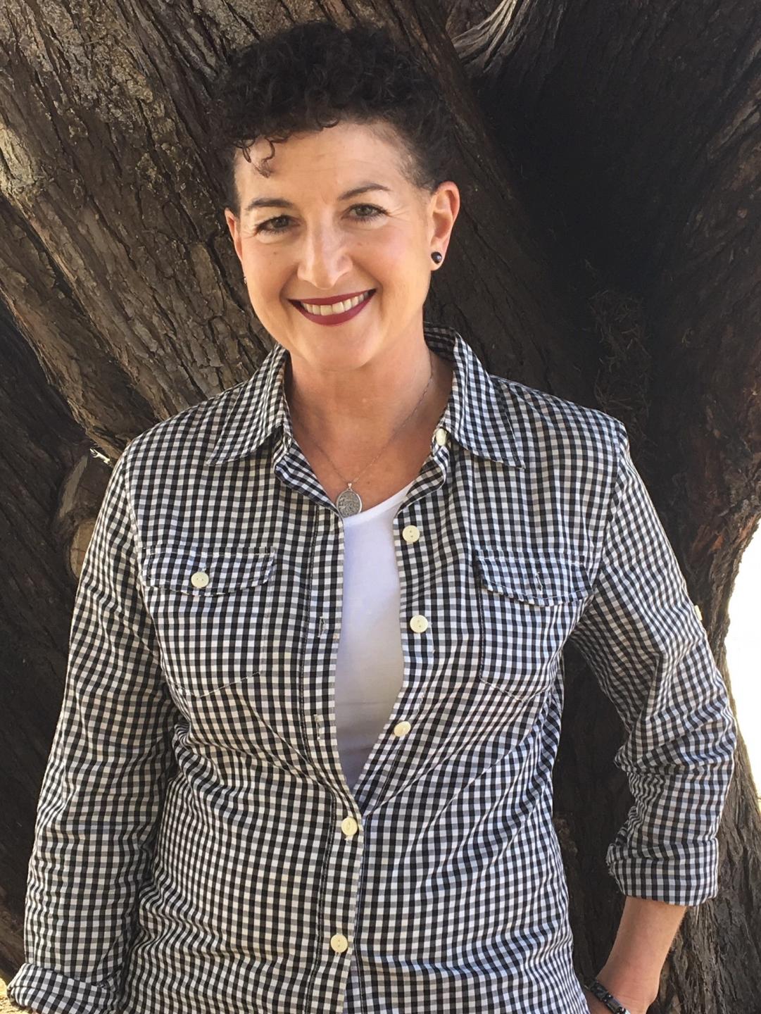 Image of Jordana Ybarra-Telias, a smiling woman with short, curly, dark hair, wearing a black and white plaid button-down shirt.