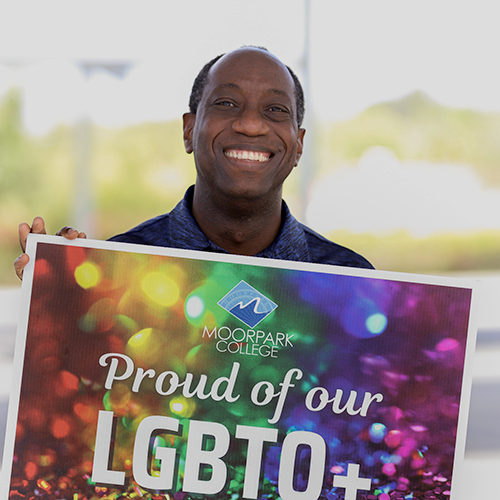 President Sokenu holds a sign that says "Moorpark College Proud of our LGBTQ+"