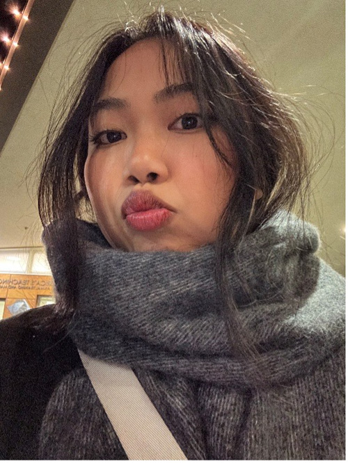 A woman with dark hair in a thick gray scarf pouts at the camera indoors.