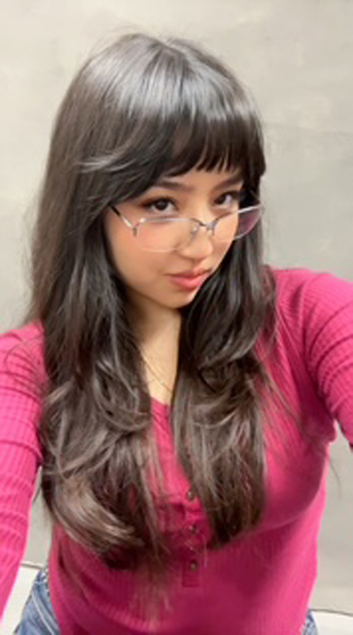 A woman in a pink top and glasses with long, wavy hair.