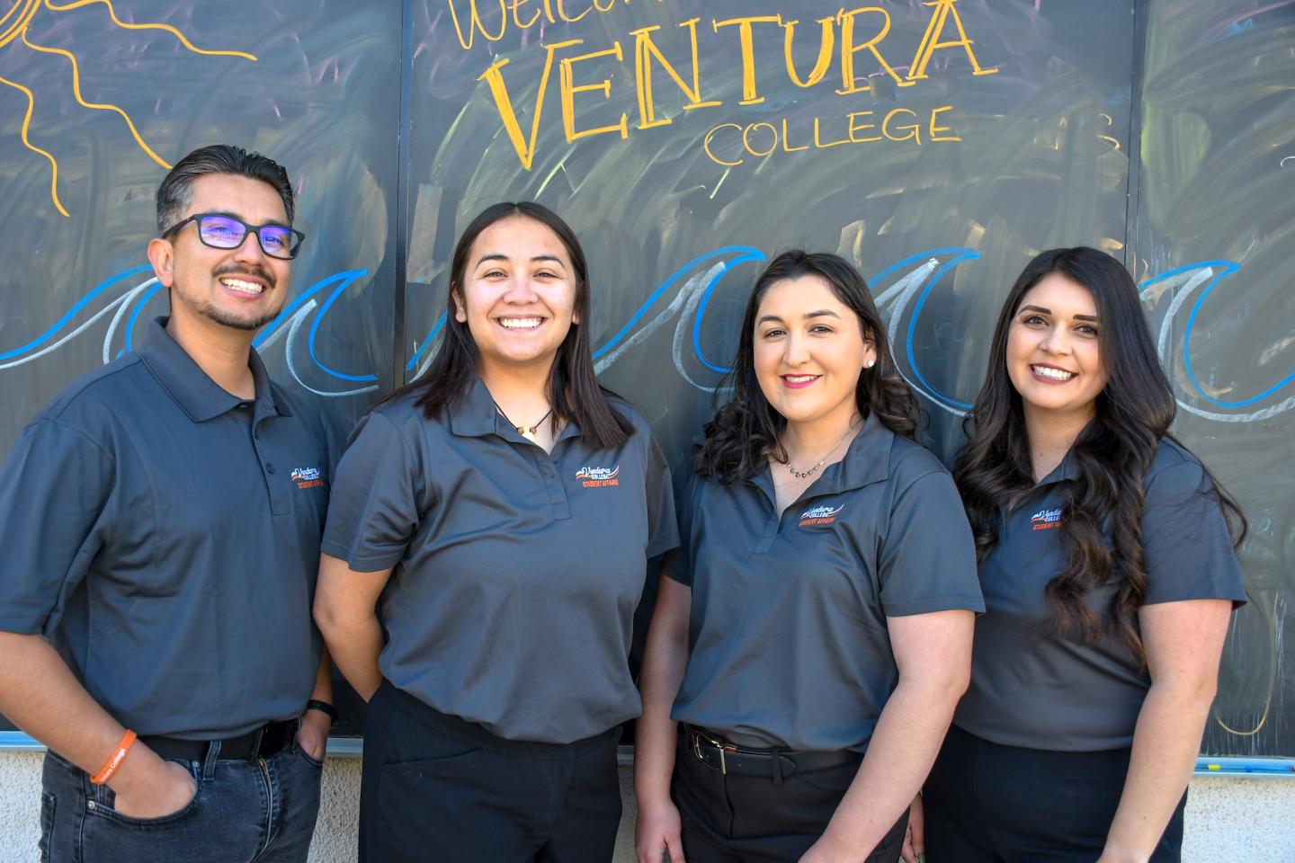 Four Ventura College outreach staff members stand smiling in matching polos in front of a chalkboard reading “Welcome Ventura College.”