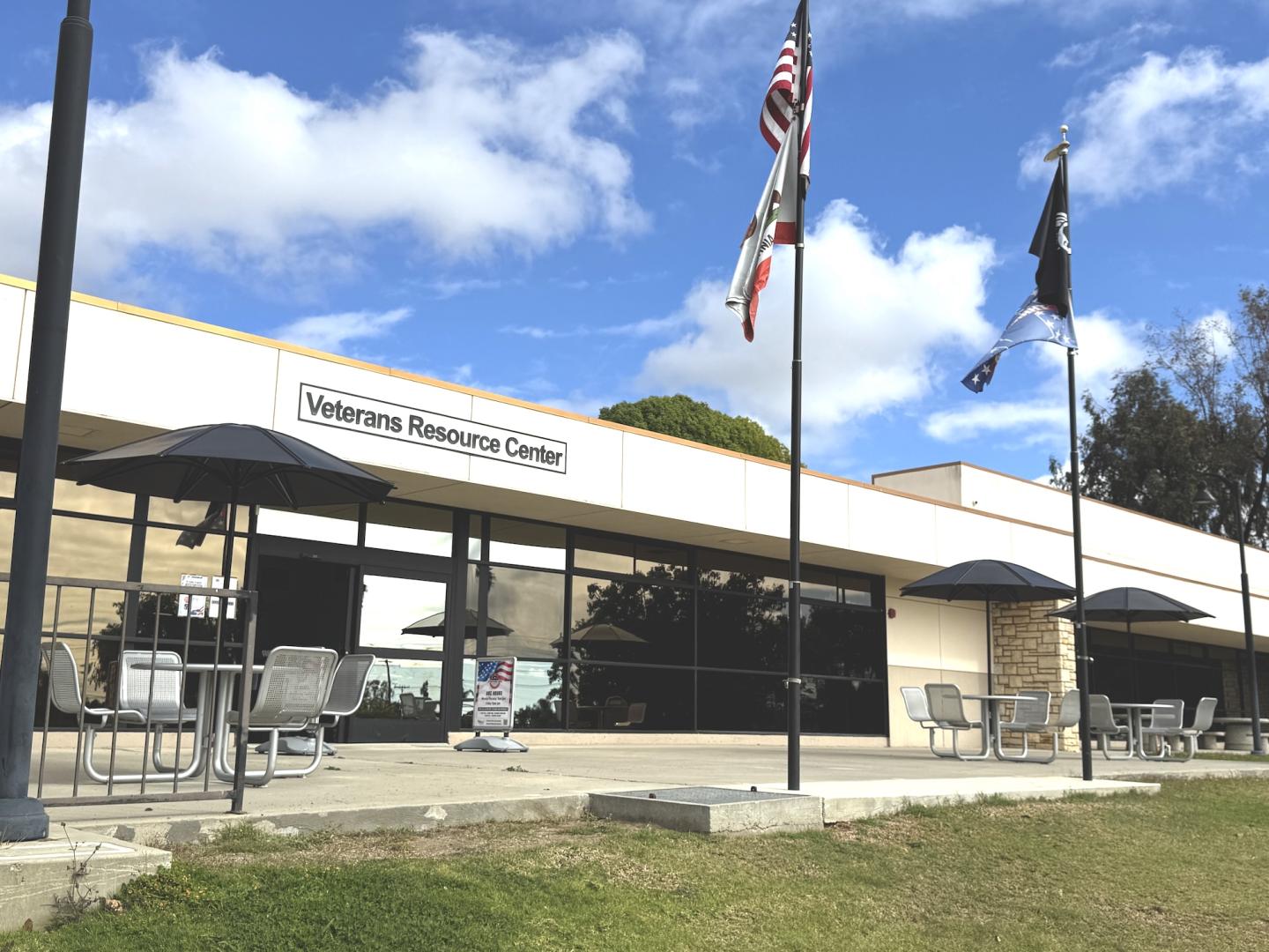 Exterior of Ventura College campus Veterans Resource Center with outdoor seating and three flags flying in front under a blue sky.
