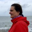 Profile of teacher wearing a red jacket with wind blowing her hair and North Sea in the background