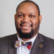 picture of dr. aaron jones in a brown suit with a colorful African bowtie