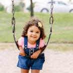 Little girl leaning on a swing at an outdoor park. 