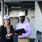 Two people wearing safety helmets, one holding a tablet and 