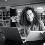 Young adult college student studying with a textbook and a laptop on a desk.