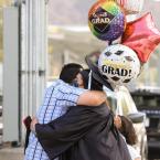 Moorpark College Graduate holding celebratory balloons and hugging another person while wearing a mask.
