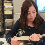 Young student wearing Oxnard College vest reading textbook in library.