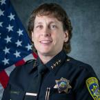 Police Chief Kelli Florman, white woman with short curly brown hair wearing her police uniform and sitting in front of an American flag