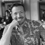 Damien Peña, a man with short dark hair wearing a floral shirt and smiling at the camera