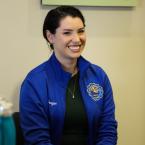 Photo of Allie Frazier, a woman with short brown hair pulled into a bun smiling, wearing a green dress with a royal blue jacket with the Oxnard College seal