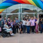Students, faculty, and staff celebrate under a rainbow arch at Oxnard College's Lavender Graduation 2026, waving pride flags and cheering outside the campus entrance.
