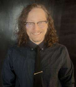 Photo of Dylan Altman. He wears a black tie and a dark-blue button up.