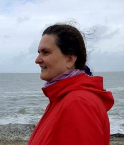 Profile of teacher wearing a red jacket with wind blowing her hair and North Sea in the background