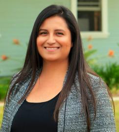 Esmeralda posing and smiling for the camera with a blue house and orange flowers background