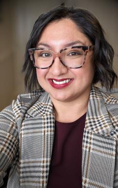 Woman wearing glasses, a purple shirt, and jacket.