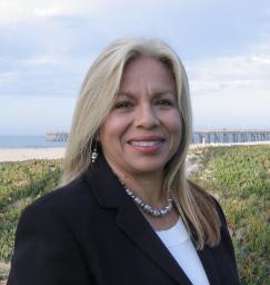 Sylvia standing at beach with pier and ocean in background.