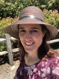 Renee Butler, brown hair, wearing a sun hat and purple blouse with white flowers
