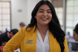 Female student with long brown hair wearing a blouse and yellow blazer in Boardroom