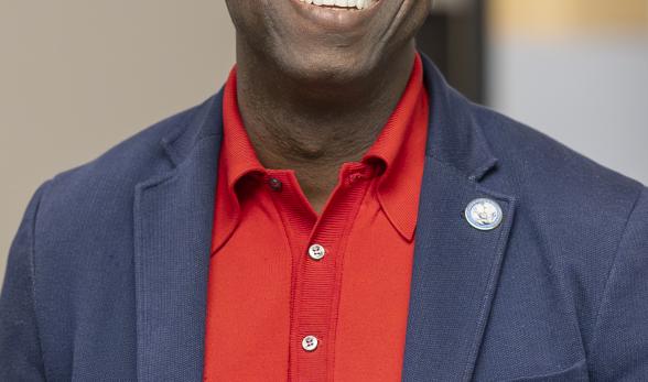 Dr. Julius Sokenu smiling, wearing a red shirt and blue spor