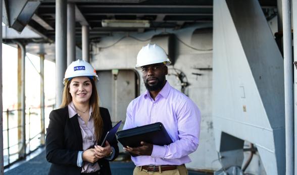 Two people wearing safety helmets, one holding a tablet and 