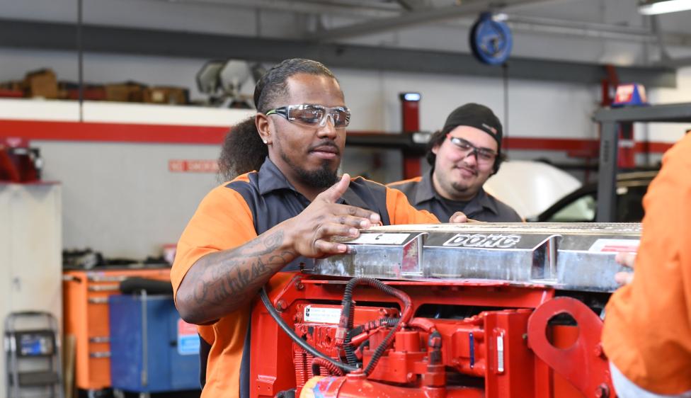 Two students wearing safety glasses work on a diesel engine in a Ventura College automotive technology lab.