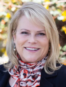 Kim Hoffmans, woman with blond hair smiling and wearing a re Kim Hoffmans, woman with blond hair smiling and wearing a re
