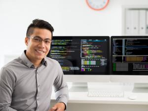 Male student is sitting at a computer with two large monitors