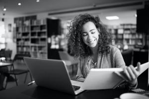 Young adult college student studying with a textbook and a laptop on a desk.