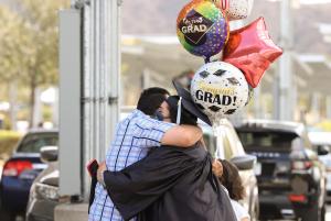 Moorpark College Graduate holding celebratory balloons and hugging another person while wearing a mask.