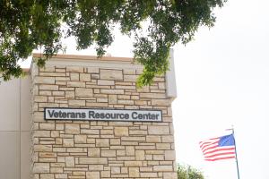 Sign on the side of a building that reads "Veterans Resource Center" with the American flag flying in the background.